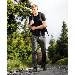 Muž s batohem kráčí po kamenité lesní cestě obklopené stromy, připravený na turistiku nebo outdoorovou aktivitu.