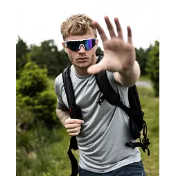 Muž s krátkými vlasy a sportovními brýlemi se zastavuje na turistické stezce v přírodě a natahuje ruku směrem k fotografovi.