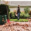 Muž čistí listí ze zahrady pomocí zahradního vysavače, vedle něj je rakev a kontejner na sběr listí.