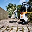Muž používá vysokotlaký čistič k čištění venkovní dlažby u zdi, přičemž zařízení STIHL je na první pláně.