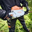Osoba drží akumulátorový plotostřih značky STIHL, připravený k práci na zahradě.