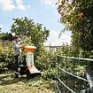 Muž v zahradě vkládá větve do zahradního drtiče větví značky STIHL, který drtí rostlinný odpad.