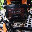Dobíjecí baterie STIHL AK 10 s indikátorem stavu nabití připevněná na zahradním nářadí, pokrytá kapkami vody.