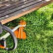 Sečení trávy pod dřevěnou zahradní lavicí pomocí motorové strunové sekačky.
