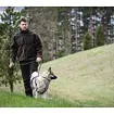 Muž v outdoorovém oblečení vede na vodítku psa, stojí na louce s lesem v pozadí.