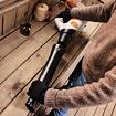 Osoba v rukavicích drží a připravuje aku foukač listí značky STIHL na dřevěném stole v dílně.