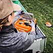 Žena v pracovním oblečení vkládá baterie do dobíjecí stanice STIHL, vedle ní leží travní akumulátorový vyžínač položený na trávníku.
