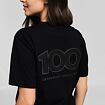 Žena otočená zády, na černém tričku nápis 100 s vrstvami připomínajícími letokruhy stromu a text "Legendary since 1922".