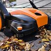 Ruční mechanický zametací stroj čistí chodník od suchých podzimních listů.